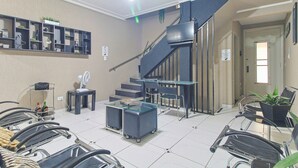 Un área de espera con sillas, una pequeña mesa, un ventilador y una escalera.