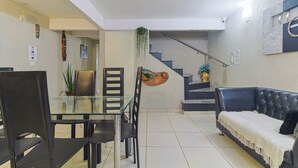 Una sala de estar moderna con una mesa de comedor de vidrio, sillas negras, un sofá de cuero oscuro y una escalera que sube a un nivel superior.