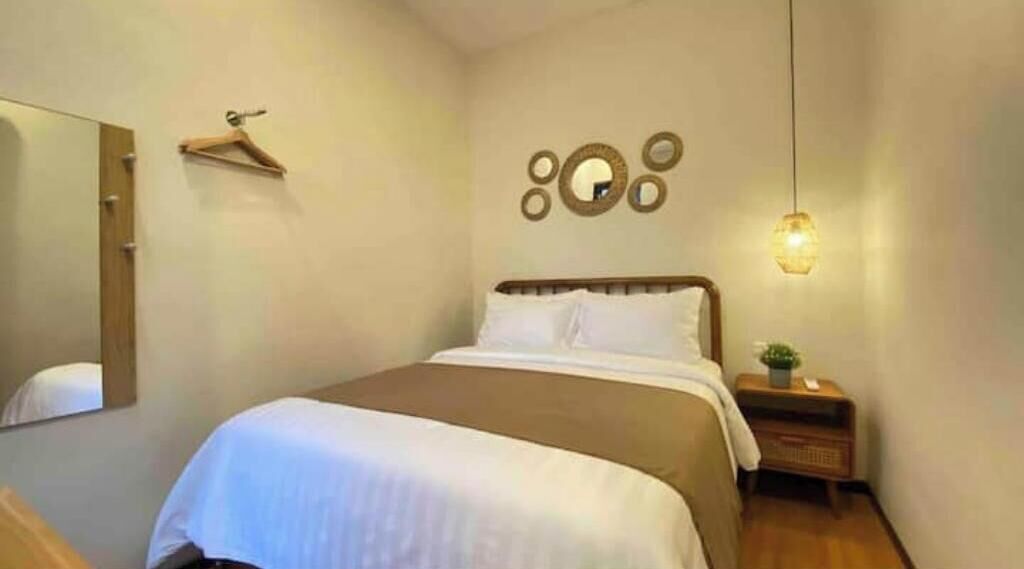 A neatly arranged bedroom with a bed, a bedside table with a lamp, a mirror, and a wall-mounted circular decoration.