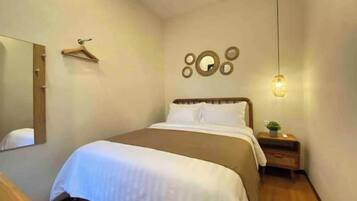 A neatly arranged bedroom with a bed, a bedside table with a lamp, a mirror, and a wall-mounted circular decoration.