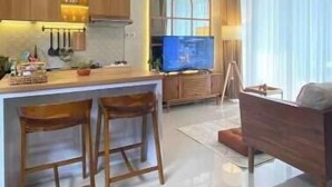 Uma cozinha moderna com armários de madeira, uma ilha central com banquetas, um ventilador de teto e uma televisão.