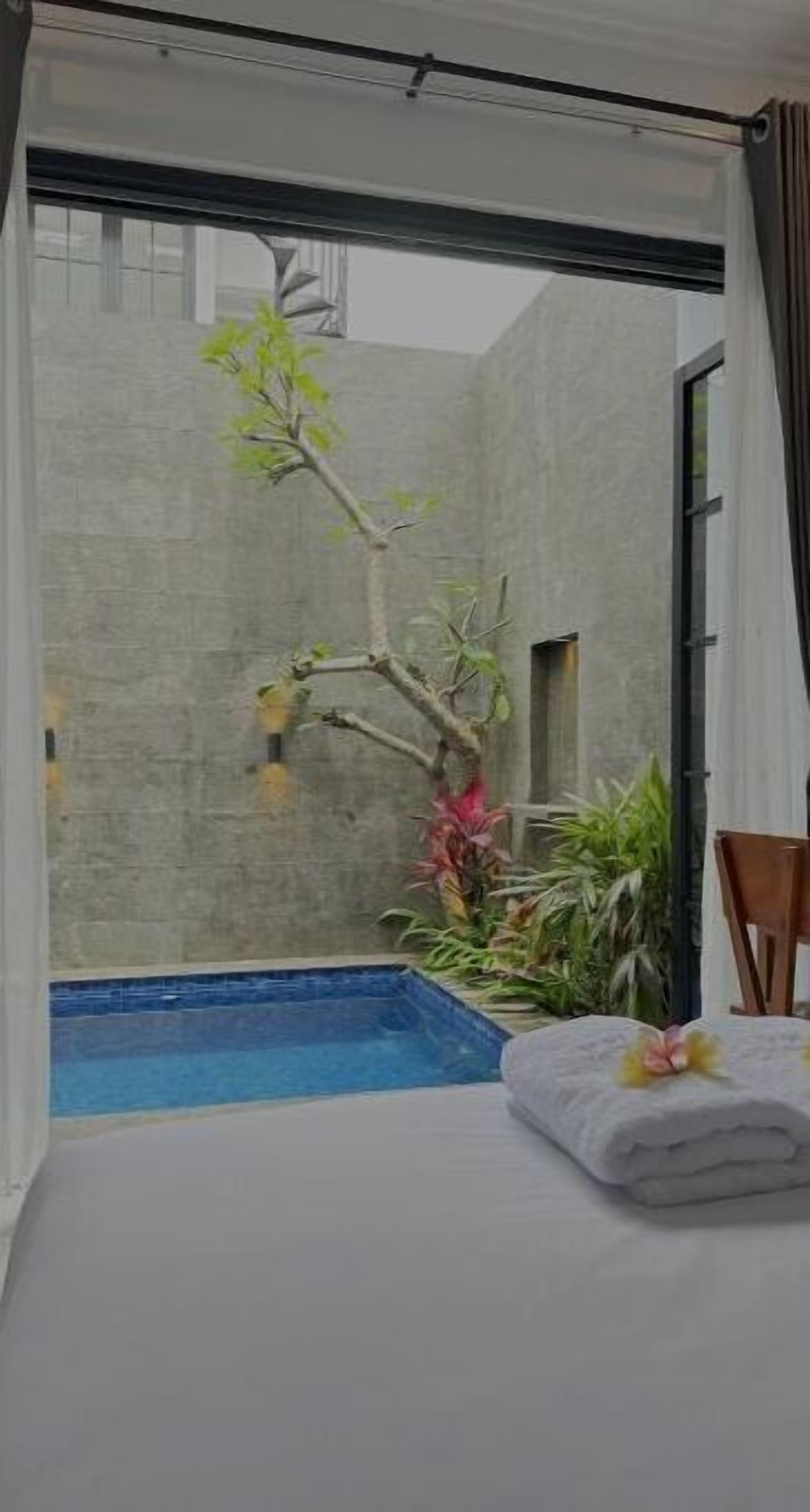 A room with a view of a swimming pool, a small tree, and a neatly folded towel on the bed.