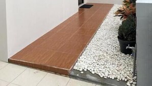 A modern building with a large window, a wooden door, and a small garden area with pebbles and plants. - The Pines Smart Homes (Batu)
