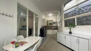 A compact kitchen with white cabinets, a dining table with chairs, and a potted plant on the counter. - Aira Villas Private Pool (Junrejo)
