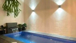 A spa area with a hot tub, wooden flooring, and wall-mounted lighting.