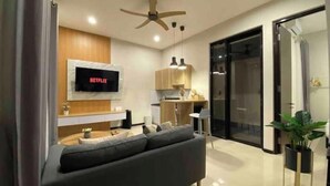 A modern living room with a grey sofa, a mounted TV displaying 'NETFLIX', wooden cabinets, and a ceiling fan.