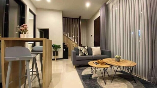 A modern living room with a sofa, coffee table, and bar stool. There is a staircase in the background leading to another level.