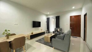 Een moderne woonkamer met een eethoek, een grijze bank, een flatscreen televisie en een houten salontafel.