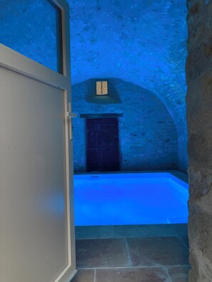 A stone-walled room with a large bathtub, a wooden door, and a small window.