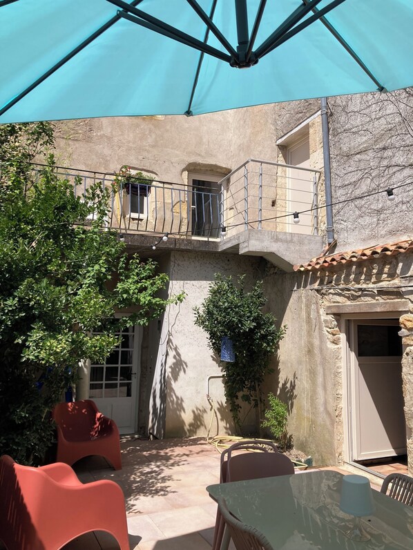 Un patio con una mesa, sillas, un paraguas azul y un edificio con balcón.