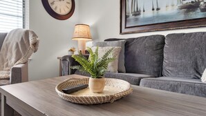Una sala de estar con una mesa de centro de madera, una planta en maceta, una lámpara, un reloj y un cuadro con barcos de vela.