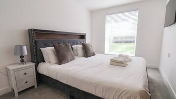 A bedroom with a bed, bedside table, lamp, and a window with blinds.