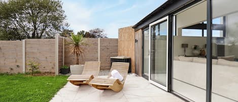 A patio with two wooden lounge chairs, a small palm tree, and a tiled floor.