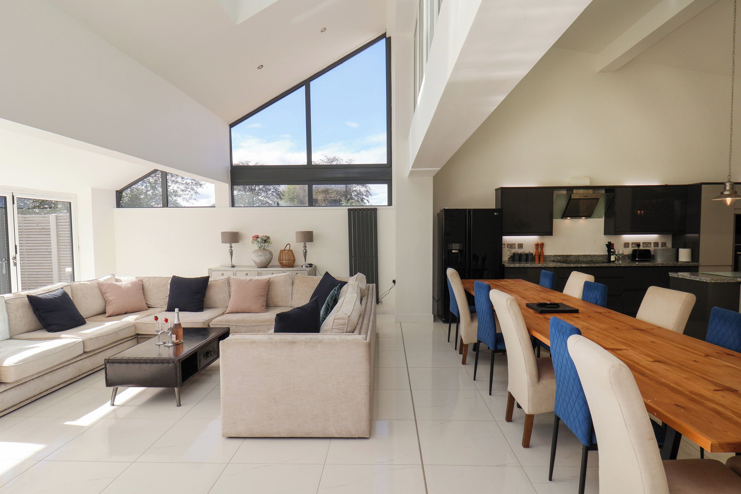 A modern living room with a large sofa, a dining table, and a kitchen area with a refrigerator and stove.