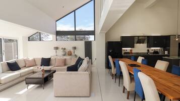 A modern living room with a large sofa, a dining table, and a kitchen area with a refrigerator and stove.