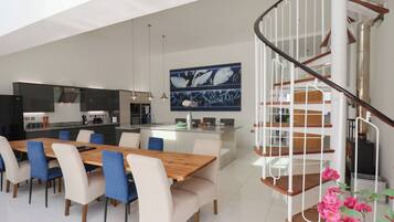 A modern kitchen with a central island, a dining area with a wooden table and chairs, and a spiral staircase.