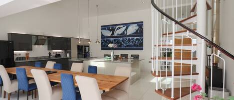 A modern kitchen with a central island, a dining area with a wooden table and chairs, and a spiral staircase.