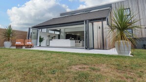 A modern house with a patio area, a large potted plant, and a wooden bench. - Meadow View (Beverley)