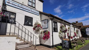 Un pub tradicional con un letrero que dice 'The Ferguson Fawssitt' y mesas al aire libre, con un cartel que indica servicio de comidas los 7 días de la semana.