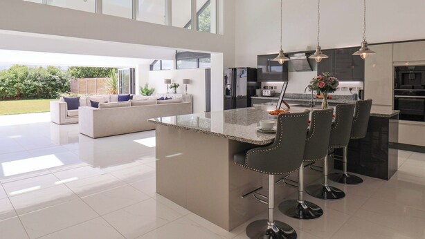 A modern kitchen with a large island, bar stools, and a dining area with a sofa. - Meadow View (Beverley)