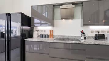 A modern kitchen with a black refrigerator, stainless steel cabinets, a built-in oven, and a granite countertop.