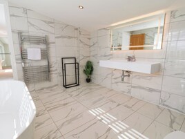 Un baño moderno con piso de mármol, un lavamanos blanco, un espejo y un perchero para toallas.