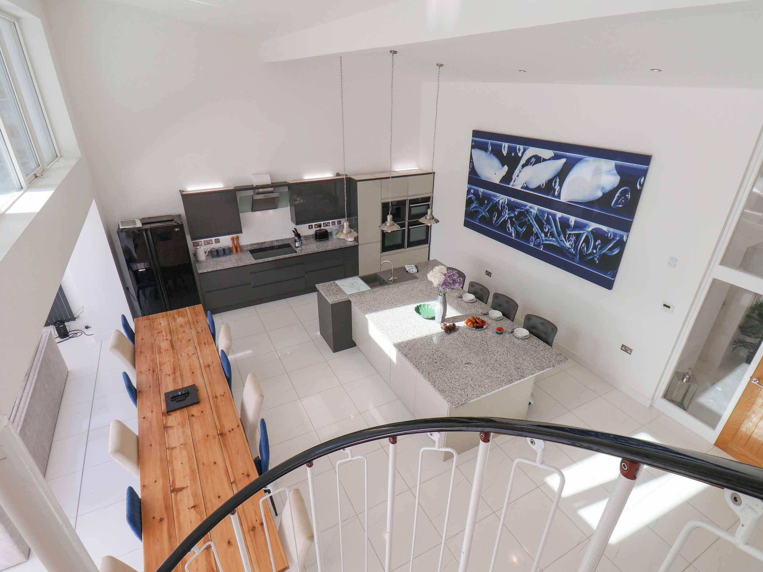 A modern kitchen with a central island, a dining area with a wooden table, and a large artwork on the wall.