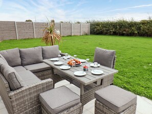 Un patio con un conjunto de comedor de mimbre, que incluye una mesa y sillas, con un plato de comida y vasos encima.