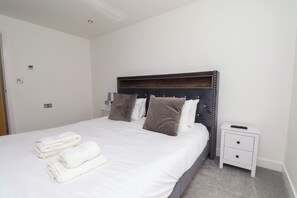 A neatly made bed with white linens and two pillows, a bedside table with a remote control, and a wall-mounted thermostat. - Meadow View (Beverley)
