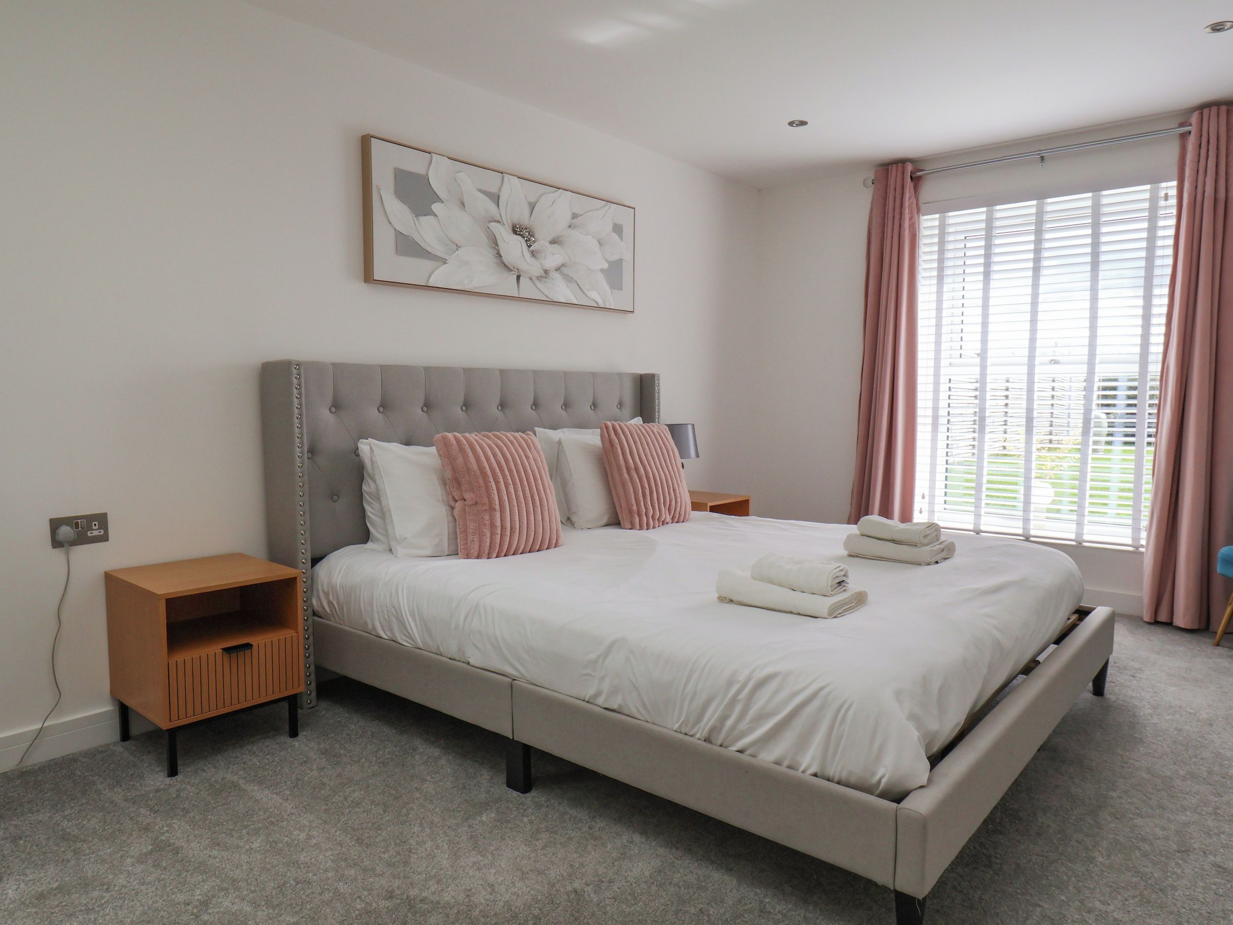 A bedroom with a large bed, a bedside table, a wall-mounted artwork, and a window with curtains.