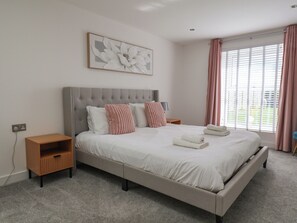 Ein Schlafzimmer mit einem großen Bett, einem Nachttisch, einem Wandbild und einem Fenster mit Vorhängen.