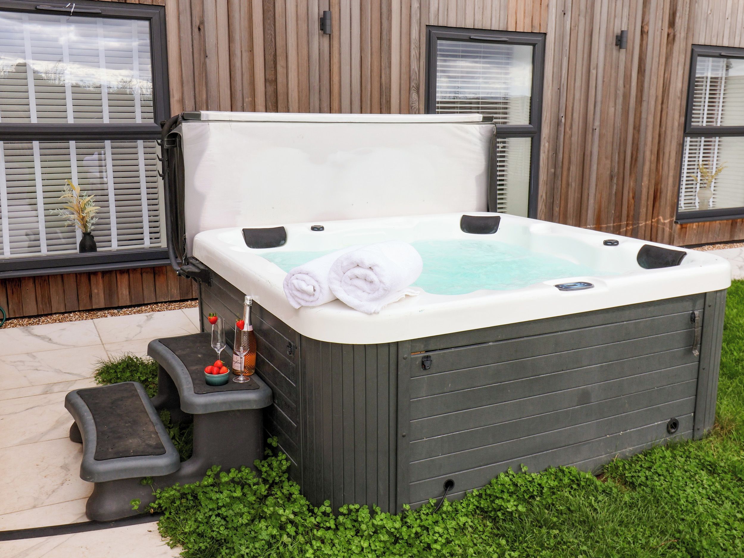 Un jacuzzi de spa con dos toallas enrolladas, una botella de champán y una copa de vino sobre una mesita auxiliar.