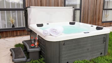 Un jacuzzi de spa con dos toallas enrolladas, una botella de champán y una copa de vino sobre una mesita auxiliar.