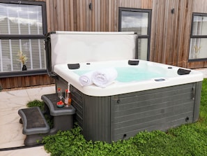 Un jacuzzi de spa con dos toallas enrolladas, una botella de champán y una copa de vino sobre una mesita auxiliar.