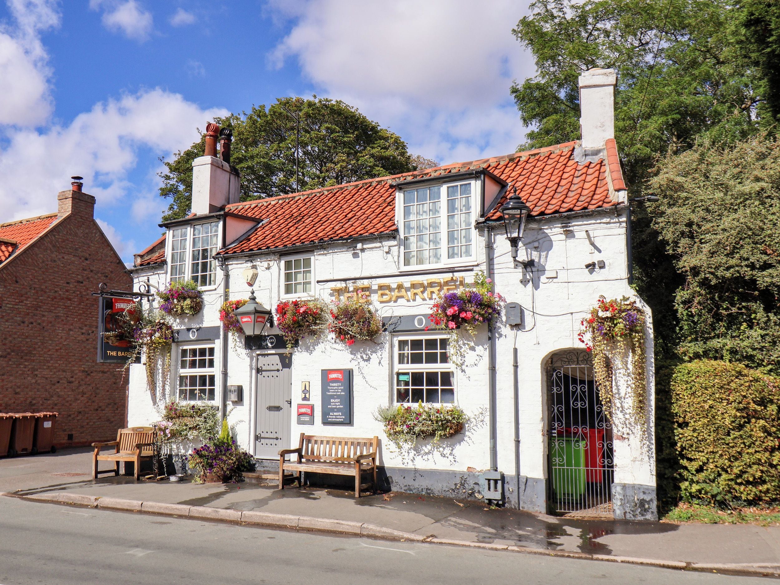 Um pub tradicional com fachada branca, telhado de telhas vermelhas e cestos com flores pendurados.