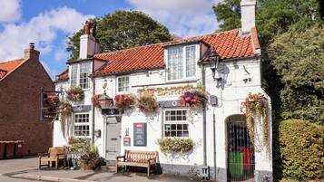 Um pub tradicional com fachada branca, telhado de telhas vermelhas e cestos com flores pendurados.