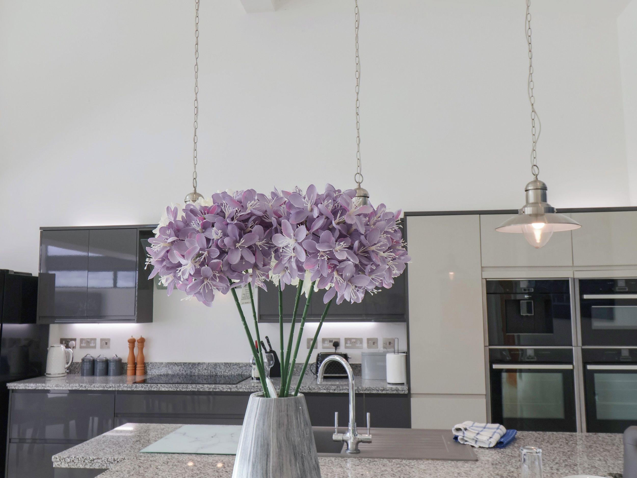A modern kitchen with a granite countertop, stainless steel appliances, and a vase with purple flowers.