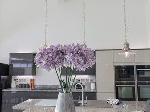 A modern kitchen with a granite countertop, stainless steel appliances, and a vase with purple flowers. - Meadow View (Beverley)