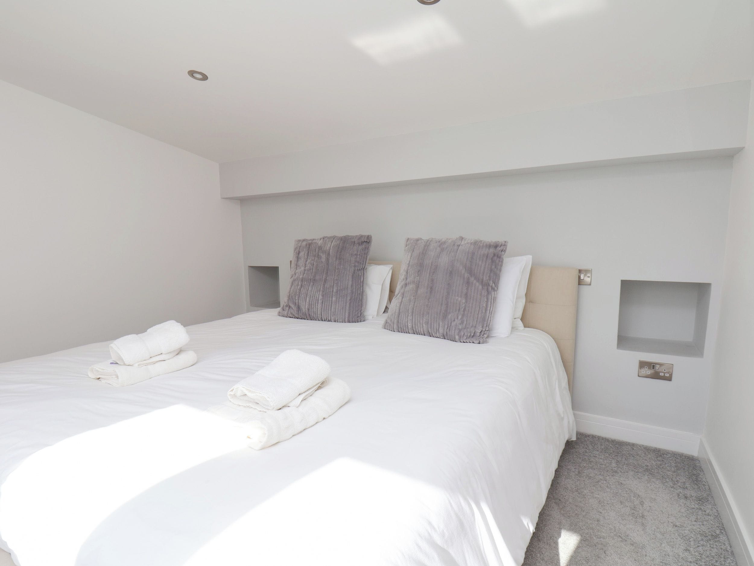 A modern bedroom with a large bed, two pillows, and neatly folded towels.