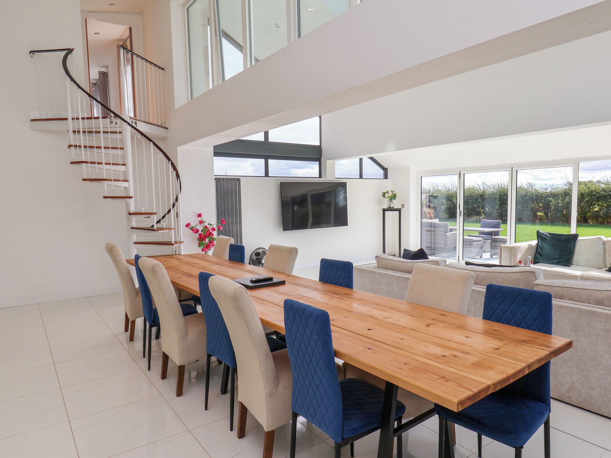 A modern dining area with a wooden table, blue upholstered chairs, and a staircase leading to an upper level.