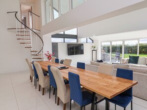 A modern dining area with a wooden table, blue upholstered chairs, and a staircase leading to an upper level. - Meadow View (Beverley)