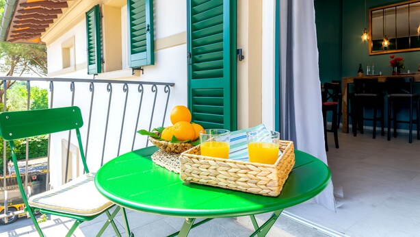 A green table with a wicker basket containing oranges and glasses of orange juice, a green chair, and a balcony railing. - La Mansarda Chic by TuscanyWeGo (Prato)