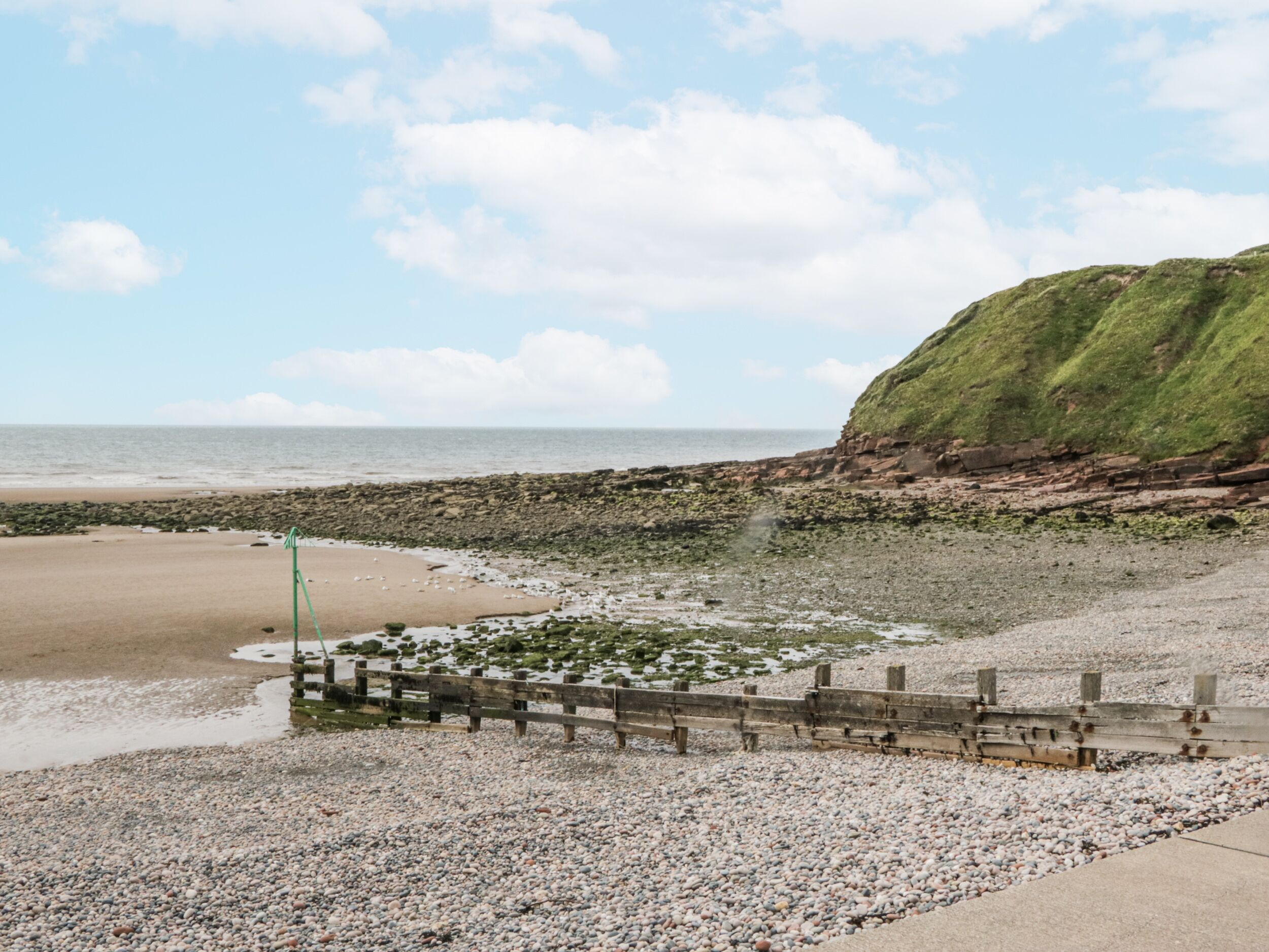 A rocky beach with a wooden fence and a grassy cliff.
