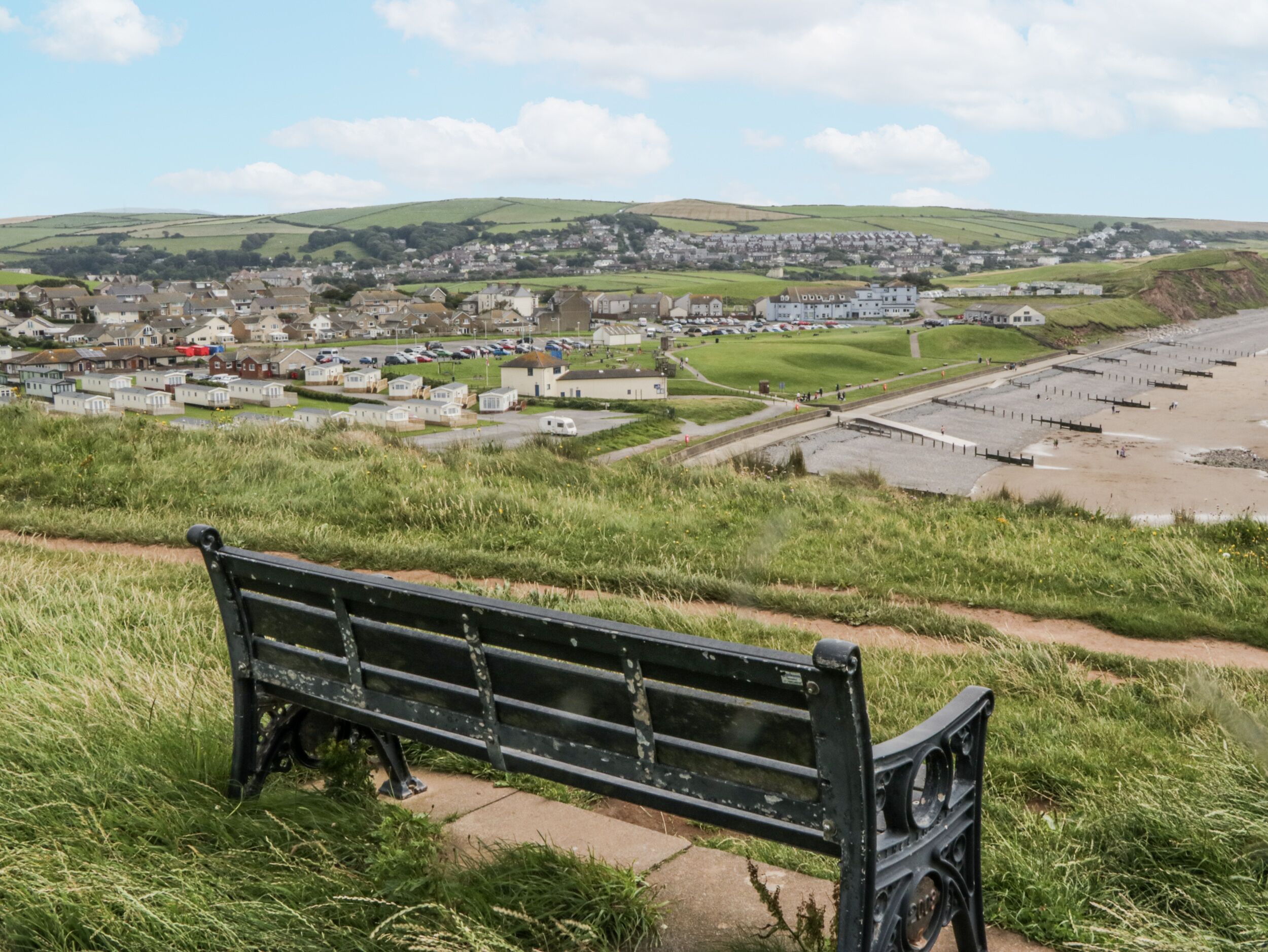 A bench overlooking a coastal town with a view of the sea and hills in the distance.