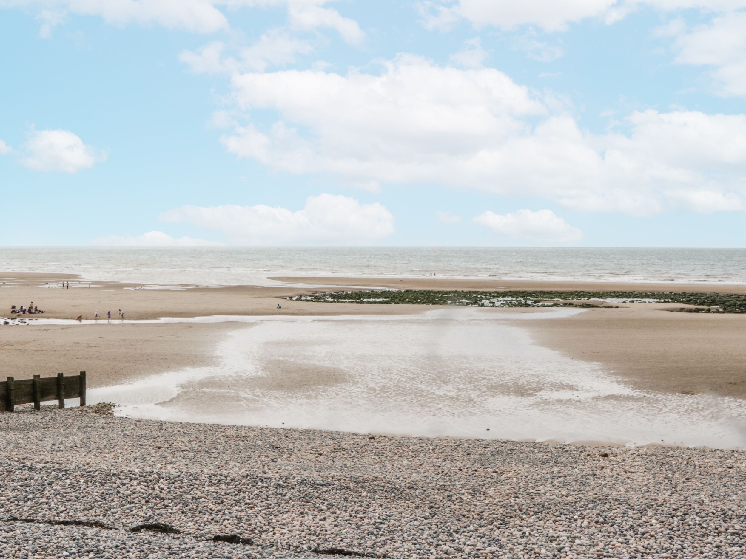 Een strand met een kiezelstrand in de voorgrond, een zandvlakte in het midden en een rustige zee op de achtergrond.