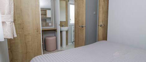 A bedroom with a bed, a wooden wardrobe, a bathroom with a sink, and a mirror.