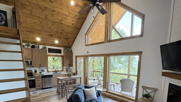 A spacious living area with a high ceiling, wooden beams, a large sofa, a television, and a fireplace.