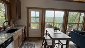 A spacious kitchen with wooden cabinets, a granite countertop, and a large window overlooking a lush landscape.