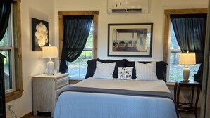 A bedroom with a bed, a ceiling fan, a window with curtains, a nightstand, a lamp, and a framed picture on the wall.