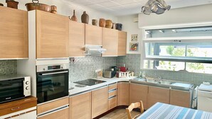 A modern kitchen with wooden cabinets, a built-in oven, a microwave, and a large window providing natural light. - House Apartment whole garden rai (Biarritz)